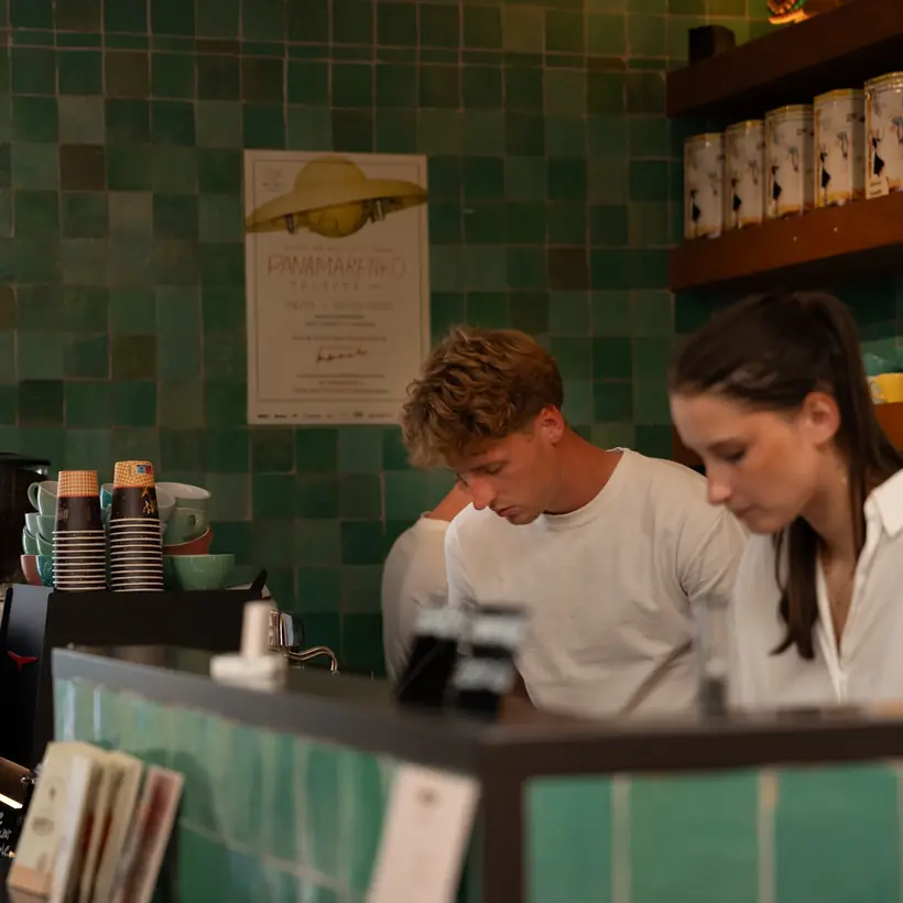 Achter de toog wordt gewerkt, met de koffieblikken op de rekken