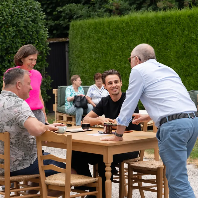 Gasten in gesprek aan een houten tafel in de tuin bij de branderij